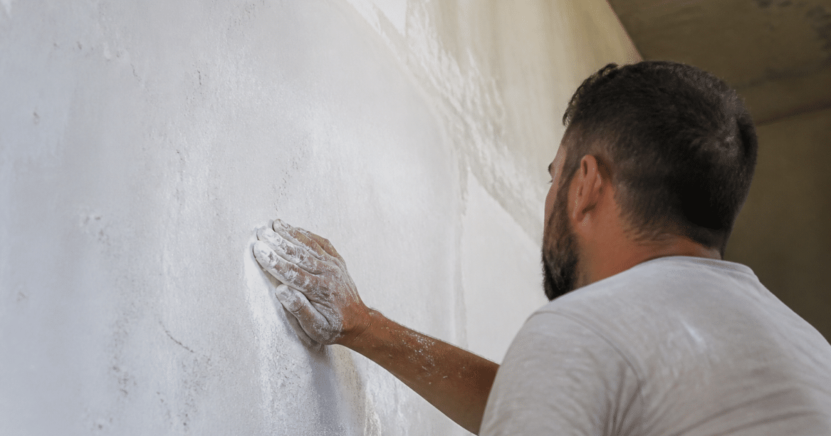 Main appliquant poudre blanche adherente sur surface platre verticale