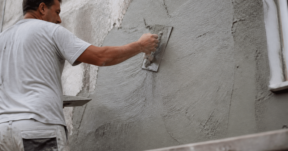 Maçon appliquant couche enduit gris mur facade existant