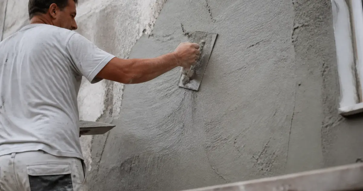 Maçon appliquant couche enduit gris mur facade existant