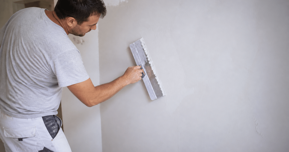 Ouvrier appliquant enduit blanc sur mur avec spatule large
