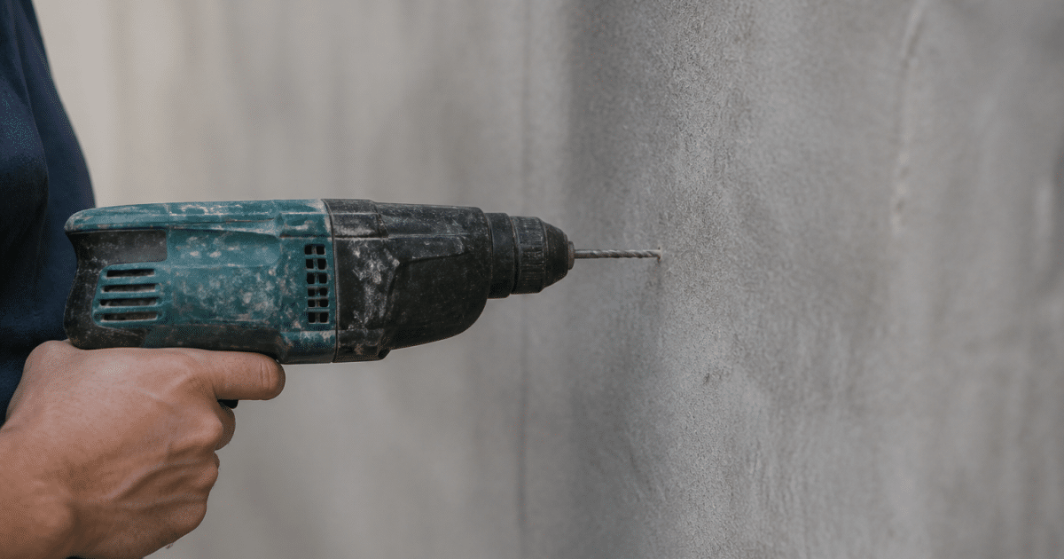 Perceuse electrique pointee contre surface grise verticale