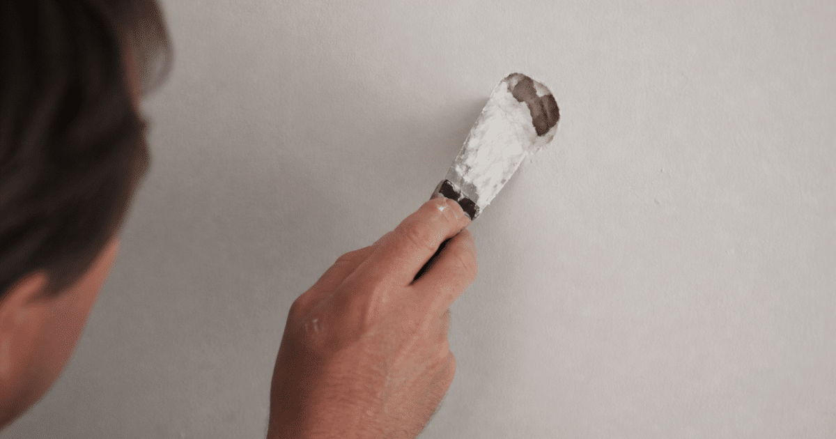 Main appliquant enduit blanc sur trou mur plâtre