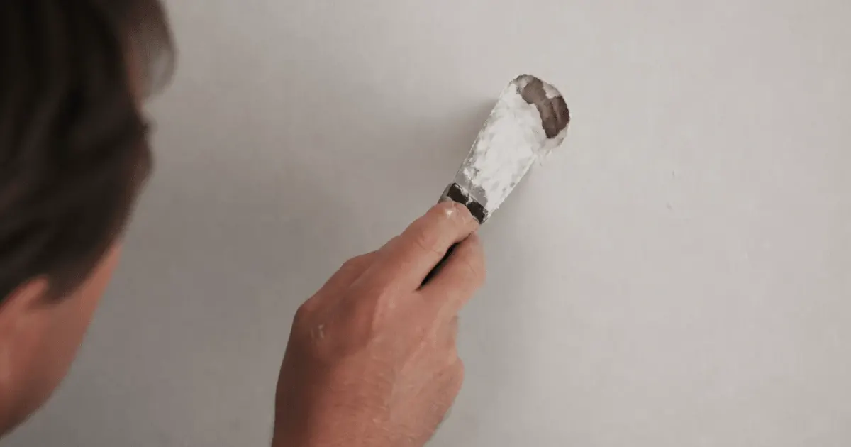 Main appliquant enduit blanc sur trou mur plâtre