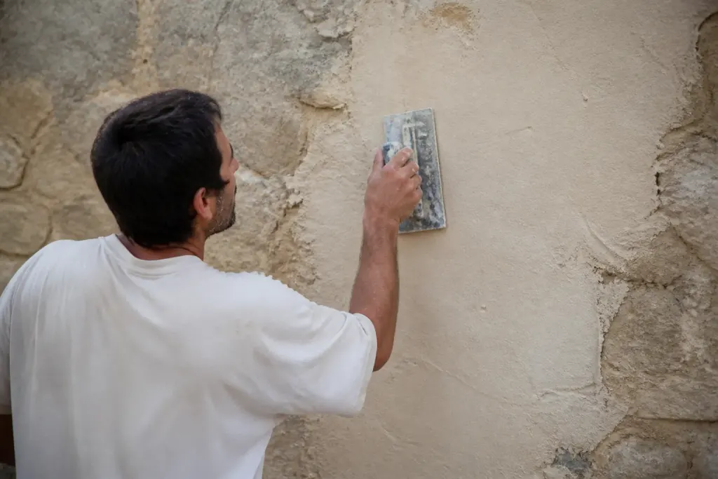 Ouvrier lissant un enduit beige sur mur ancien